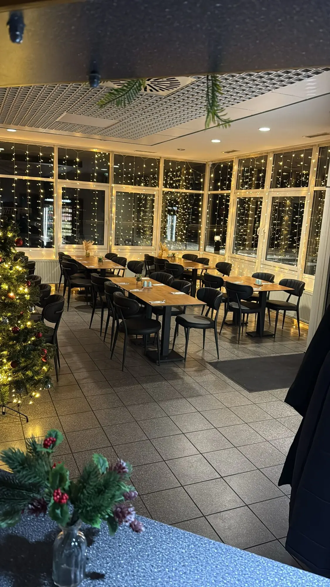 Der Gastraum am Abend: gedeckte Holztische, schwarze Stühle, Lichterketten vor der Fensterfront
